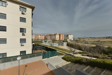 Views of an enclosed swimming pool and sports court and some residential developments at the edge of a city