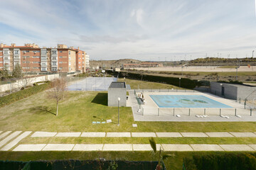 Obraz premium Views of an enclosed swimming pool and sports court and some residential developments on the outskirts of a city with gardens and stone paths