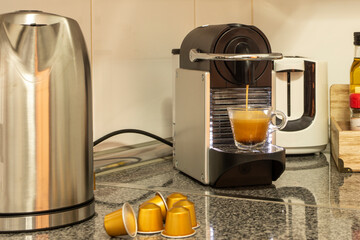Glossy granite countertop with a pod coffee machine that brews an espresso next to a hard of water