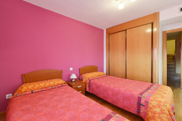 bedroom with two beds with pink walls, built-in wardrobe with sliding wooden doors