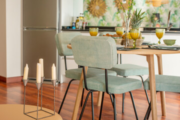 Decoration of a vacation rental home with candles on a side table next to a wooden table with breakfast of fruits and juices