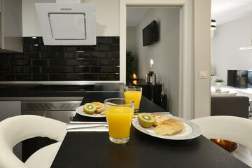 Black countertop of a kitchen with breakfast and orange juice, buns and fruits