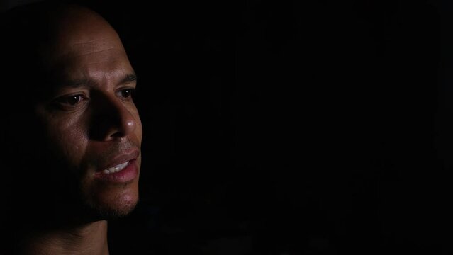 Lone man in the shadows talking to somebody off camera - could be a therapy session, argument or interrogation 