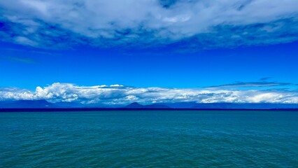 unrealistically white-gray silver Clouds on a bright blue sky a little Turquoise colorless water of the Pacific Ocean divide picture into two parts background for any title text or advertising travel