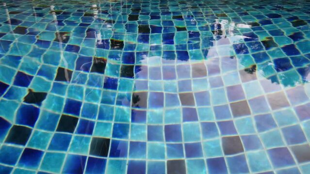 Outdoor swimming pool with the sun reflection on the surface of the water and blue porcelain tiles