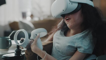 Woman with disability in a wheelchair at home wearing virtual reality glasses and holding controllers in her hands join metaverse
