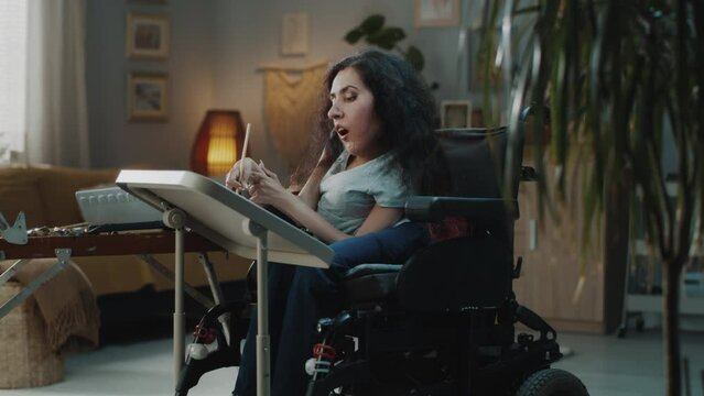 Female atrist with spinal muscular atrophy sitting in a wheelchair at cozy home and painting