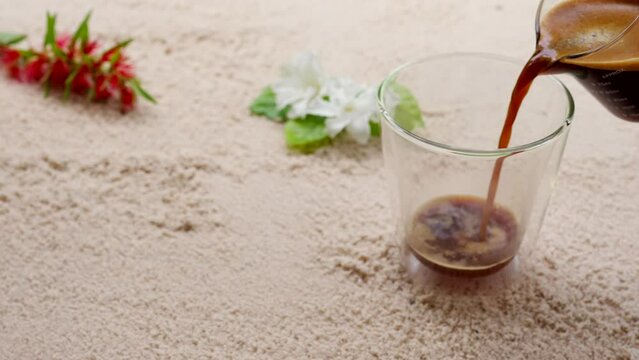 Hot coffee pouring into double wall glass on sand beach.