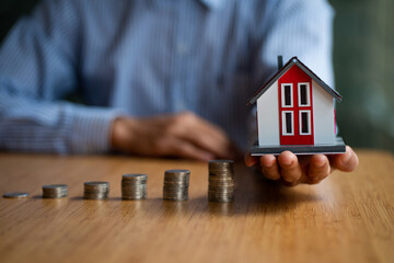 A savings accountant holds a small wooden house and a pile of coins on the table. concept of finance and savings account