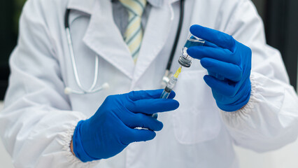 A doctor or nurse wearing blue gloves holds a bottle and a syringe of influenza vaccine and with a patient vaccine.