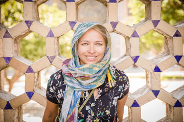 A blonde model dressed appropriately standing and smiling in front of a Central Asian wall. - obrazy, fototapety, plakaty