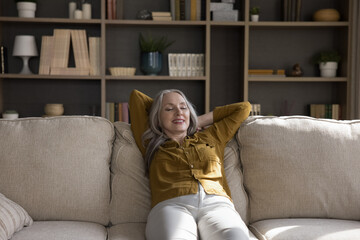 Obraz premium Cheerful relaxed mature woman resting on comfortable couch with closed eyes and happy smile, stretching body, leaning on back, enjoying comfort, leisure pause, stress relief, meditating at home
