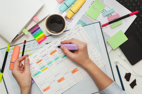 Student desk. The girl makes notes on stickers in the study schedule. The process of homeschooling or preparing homework . Top view of the table with student stationery and notes.