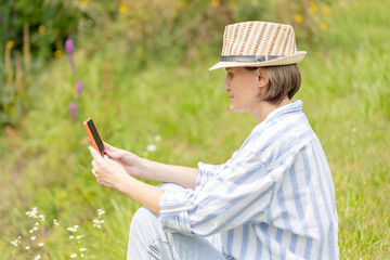 woman wearing in hat sitting in the park on the green grass with a smartphone