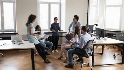 Millennial Indian employee and colleagues take part in group meeting, solve business, share ideas, discuss collaborative project, gathered in co-working workplace in modern office. Cooperation concept