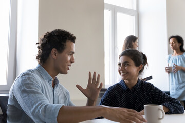 Hispanic and Indian colleagues talking seated at desk at workplace, brainstorm discuss business ideas looking motivated, working together at meeting in co-working space, cooperation, team-work concept