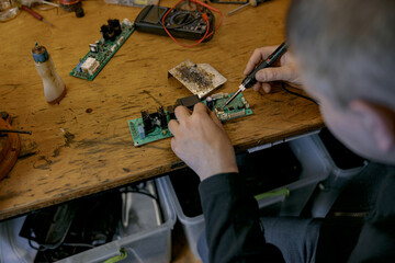 Close up of repairman hands is soldering circuit board of electronic device on the table