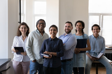 Group of happy diverse office employees pose at workplace look at camera, ready for negotiations. Multiracial company staff, professional members, motivated, successful businesspeople portrait concept