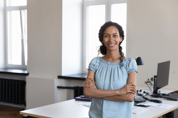 Confident African female staff member, pose in co-working office with arms crossed, smile look at...