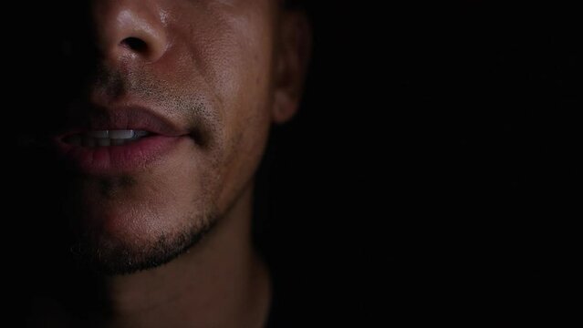 Close up shot of male mouth half lit in the shadows talking to camera, in slow motion