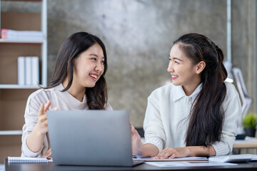 Two Asian businesswomen use laptops and smartphones in an open space office. Business concept. Data analysis, roadmap, marketing, accounting, auditing.
