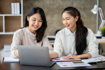 Two Asian businesswomen use laptops and smartphones in an open space office. Business concept. Data analysis, roadmap, marketing, accounting, auditing.