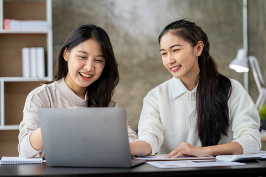 Two Asian businesswomen use laptops and smartphones in an open space office. Business concept. Data analysis, roadmap, marketing, accounting, auditing.