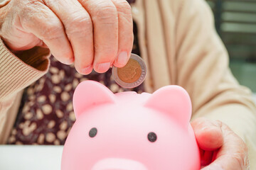 Retired elderly woman putting coins money in piggy bank and worry about monthly expenses and...