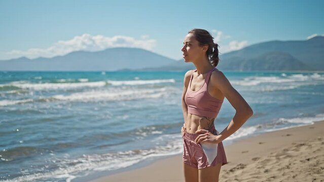 young active sporty athlete smiling woman is taking a break after making running and jogging workout on sea sandy beach with seascape at morning. go everywhere, active lifestyle concept