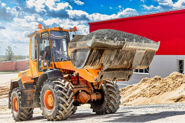 A large front loader transports crushed stone or gravel in a bucket at a construction site or concrete plant. Transportation of bulk materials. Construction equipment. Bulk cargo transportation.