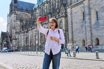Woman tourist taking a selfie in front of an ancient European cathedral - obrazy, fototapety, plakaty