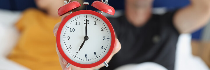 Red alarm clock against the background of a sleeping couple