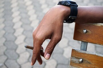 Braune schlanke elegante Hand von asiatischem jungem Mann mit Zigarre und schwarzer Uhr an...