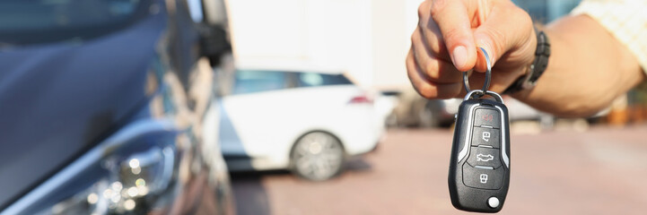 A hand near the car holds an electronic key, close-up