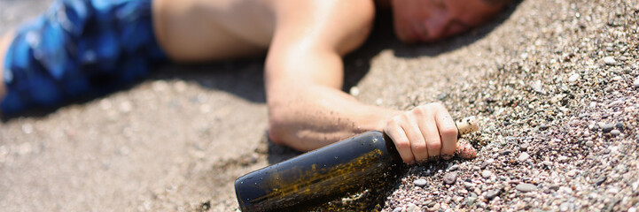 A drunk man with a bottle lies on the wet sand, blurry - obrazy, fototapety, plakaty