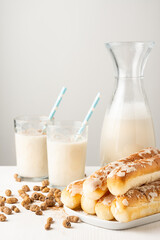 Close-up of bottle and glasses of horchata with straw, on table with tiger nuts and fartons, white background, vertical