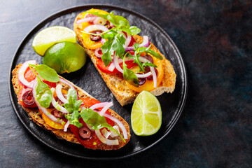 Vegetarian sandwiches on a dark background. Spanish tapas with vegetables, greens, olives and lime. Healthy sandwiches on a black plate. Top view. Copy space