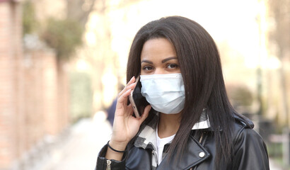 Health, safety and pandemic concept. Young woman wearing black face protective reusable barrier mask outdoors calling on smartphone.