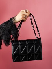 Hand of woman holds black leather bag on pink background