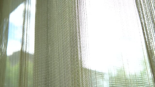 Blurred view of the sun, peeking from the window in the room through the curtain and glass of a window. The concept of a brand new day and a happy world. Defocused low angle shot.