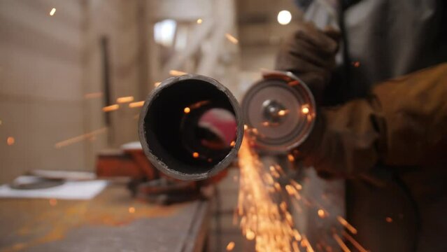Male hand cutting off pieces of water pipe with angle grinder. Cutting of a steel with splashes of sparks at construction site. Sparks during cutting of metal angle grinde