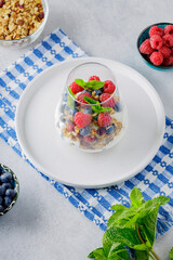 Glass with granola, yogurt, fresh raspberries, blueberries and mint. High protein and diet breakfast on a white-blue napkin. Healthy food concept
