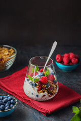 Layered cream dessert on a dark background. Homemade yogurt with granola, blueberries and raspberries. Yogurt parfait on a burgundy napkin
