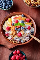 Bowl of homemade granola with yogurt and fresh berries on wooden background. Healthy breakfast with yogurt, granola and fruits on cutting board. Flat lay