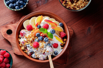 Bowl of homemade granola with yogurt and fresh berries on wooden background. Healthy breakfast with yogurt, granola and fruits on cutting board. Flat lay