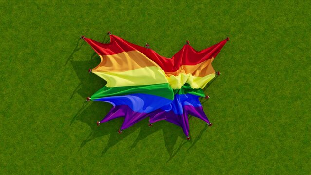 Aerial video above a unfurling LGBT Pride flag on green grass