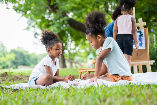 African American little girls with curly hair painting watercolor in summer park. Kid artist painter draw pictures outside.Education learning outdoor concept