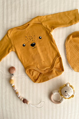 A flat lay with cute newborn baby clothes and eco-friendly accessories on a light sheet in the crib. Online fashion store, online shopping branding concept. Bodysuit, rattle, nipple clothespin, bib