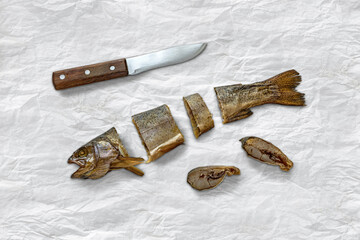 Sliced smoked fish, knife on white paper. Dried kippered trout fish
