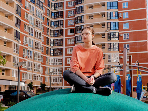 A young girl student in glasses sits in the courtyard of the new high-altitude knowledge